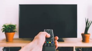 person pointing remote at a television between two potted plants