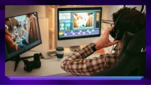 Image showing a man editing a video on two computer screens and wearing headphones. There is a purple border around the image.