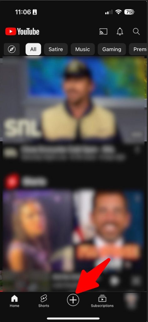 Blurred image of a home screen on a YouTube mobile app with red arrow pointing to the “+” button