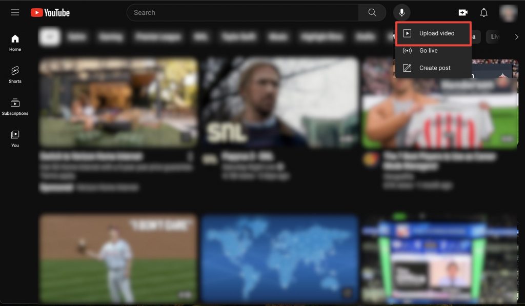 Blurred image of a YouTube home screen on a web browser, with “Upload video” highlighted.