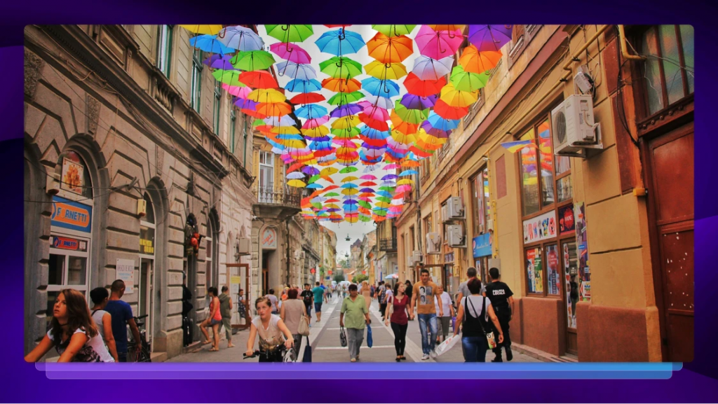 Street full of people of various cultures, being shaded by a rainbow of umbrellas.